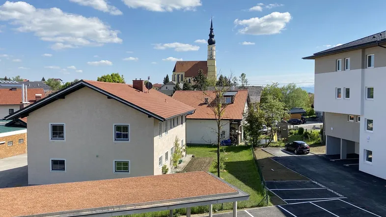 Blick auf die Wohnanlage mit Parkplätzen, Carports und einer Kirche im Hintergrund unter blauem Himmel.