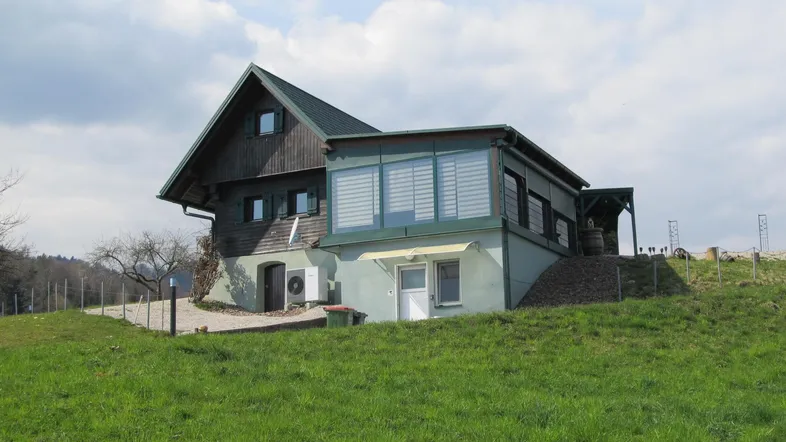 Ländliches Haus mit grünem Dach und Anbau auf einem grasbewachsenen Hügel.