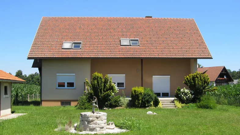 Rückansicht des Hauses mit gepflegtem Garten, Zierbrunnen und weitem Blick auf die umliegenden Felder.