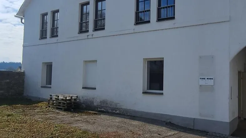Weißes Gebäude mit mehreren Fenstern und runden Akzentfenstern unter blauem Himmel.