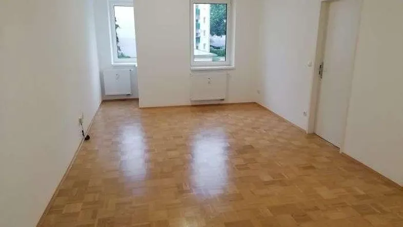 Helles, leeres Zimmer mit Parkettboden und zwei Fenstern, bereit zur individuellen Gestaltung.