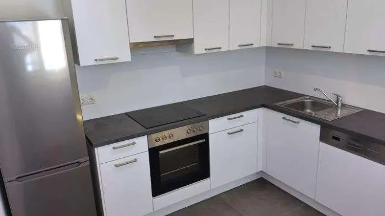 Moderne Küche mit weißen Schränken, dunkler Arbeitsplatte und integrierten Geräten.