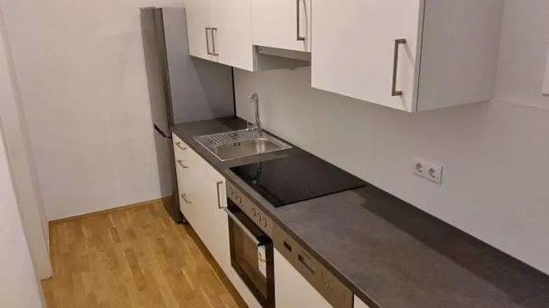 Moderne Einbauküche mit weißen Schränken, dunkler Arbeitsplatte und integrierten Geräten.