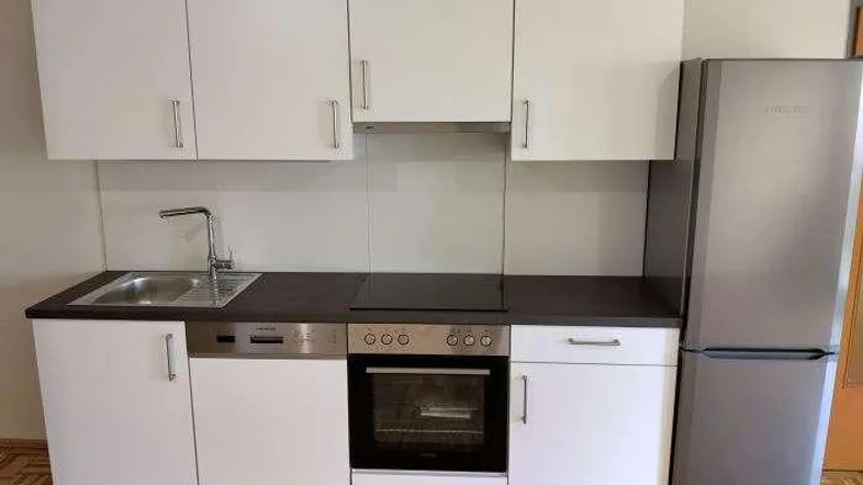 Moderne Küchenzeile mit weißen Schränken, integrierten Geräten und einem Kühlschrank.