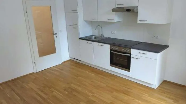 Moderne Küchenzeile mit weißen Schränken, integriertem Backofen und hellem Holzplankenboden.