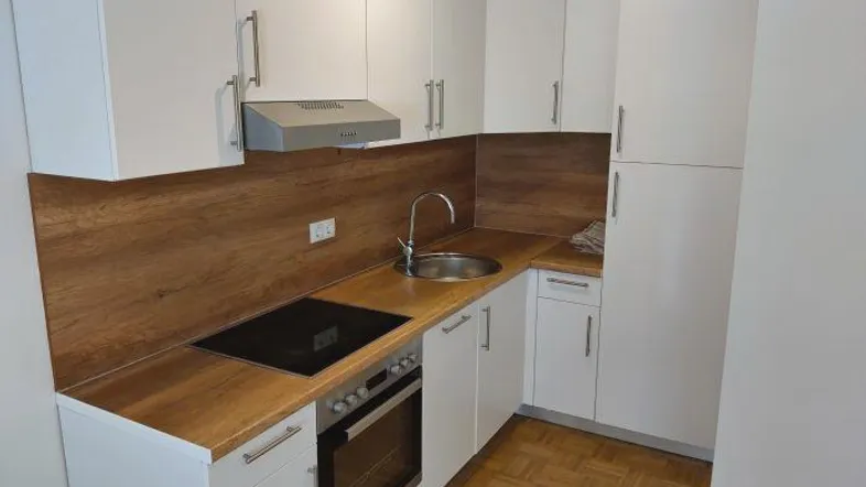 Moderne Einbauküche mit weißen Schränken, Holzoptik-Arbeitsplatte und Parkettboden.