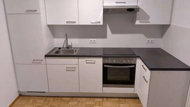 Kompakte Einbauküche mit weißen Schränken, dunkler Arbeitsplatte und integrierten Geräten.