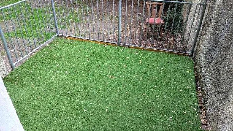 Kleine Terrasse mit Kunstrasen und Metallgeländer, umgeben von einer Mauer.