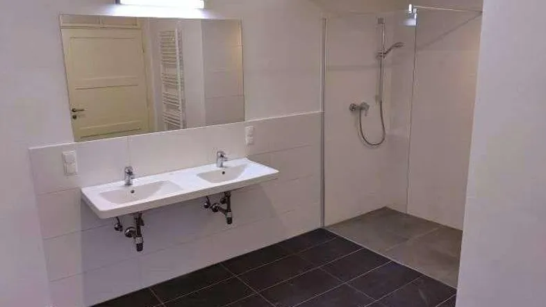 Modernes Badezimmer mit Doppelwaschbecken, großer Dusche und dunklen Fliesen.