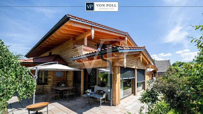 Charmantes Holzhaus mit großer gepflasterter Terrasse, Gartenmöbeln und Sonnenschirm unter blauem Himmel.