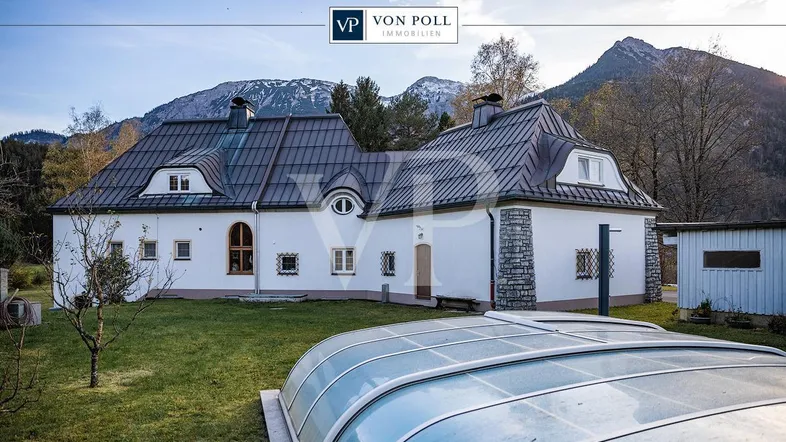 Weißes Landhaus mit Mansarddach, umgeben von einem gepflegten Garten und Bergblick, inklusive Poolabdeckung.