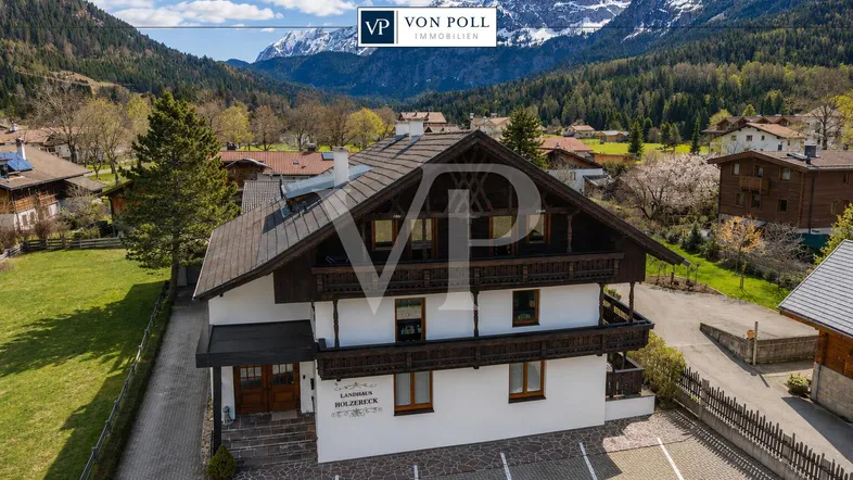 Traditionelles Landhaus im alpinen Stil mit Bergblick und Parkplätzen vor dem Gebäude.