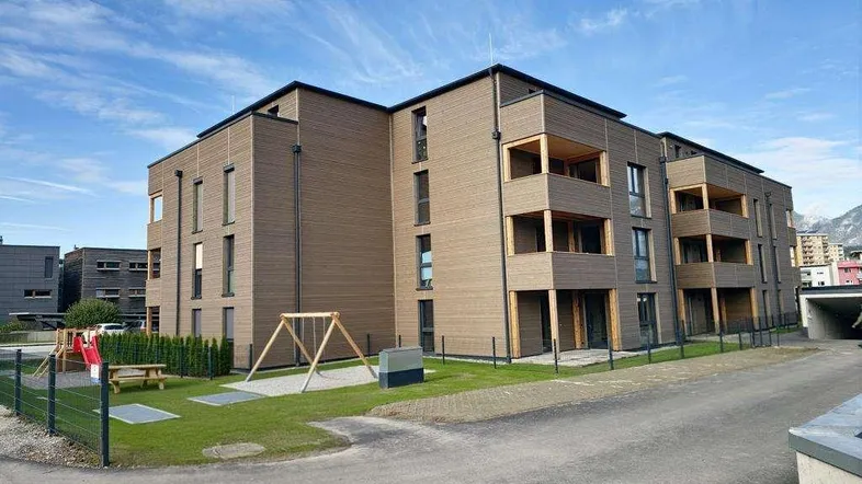 Modernes Mehrfamilienhaus mit Holzfassade, Balkonen und kleinem Spielplatz im Außenbereich.