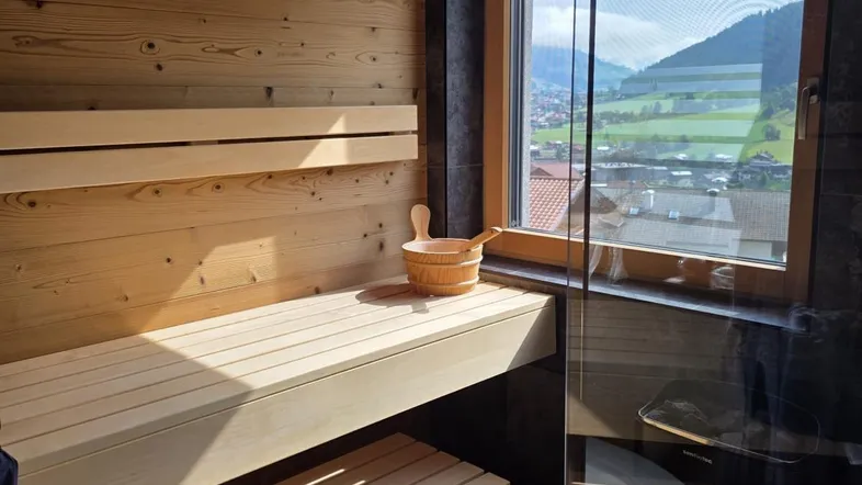 Moderne Sauna mit Holzwänden und Bänken, bietet einen schönen Blick auf die umliegende Berglandschaft.