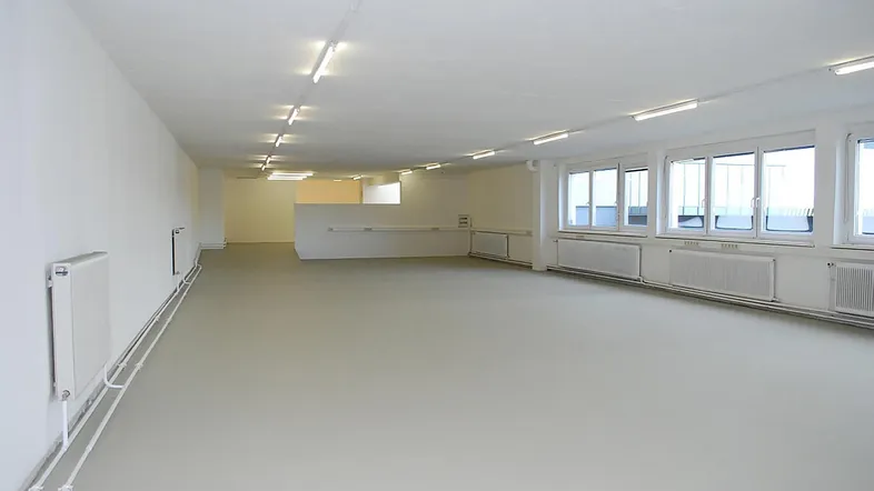 Großer, heller Büroraum mit vielen Fenstern, Heizkörpern und funktionaler Deckenbeleuchtung.