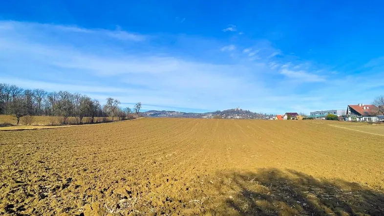 Weitläufiges Ackerland unter einem klaren blauen Himmel mit entfernten Häusern und Hügeln am Horizont.