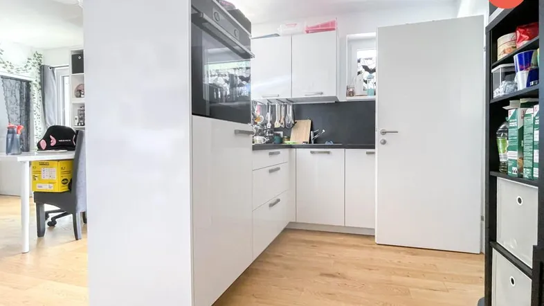 Moderne Küche mit weißen Hochglanzfronten, integriertem Backofen und Holzboden.