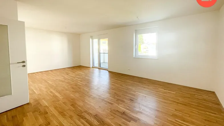 Helles, geräumiges Wohnzimmer mit Parkettboden, weißen Wänden und Zugang zum Balkon.