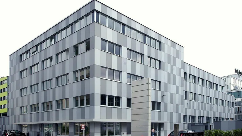 Modernes Bürogebäude mit markanter Fassade aus grauen und hellgrauen Paneelen und großen Fenstern.