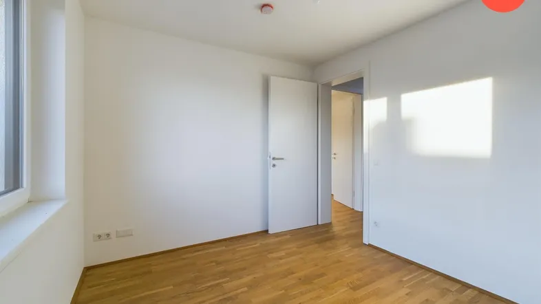 Helles Zimmer mit Holzparkettboden und einem Fenster, das viel Tageslicht hereinlässt.