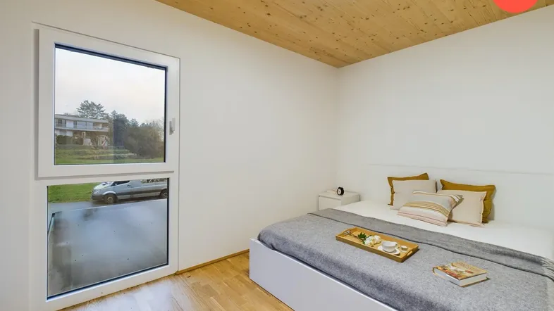 Helles Schlafzimmer mit Holzboden und Holzdecke, ausgestattet mit einem bequemen Bett und Blick ins Grüne.