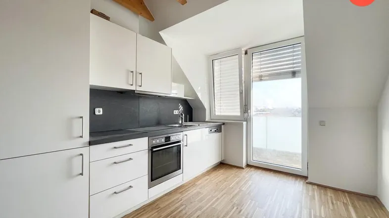 Moderne Küche in Dachgeschosswohnung mit weißen Schränken, Einbaugeräten und Zugang zum Balkon.