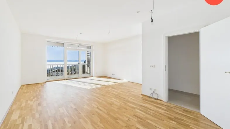 Helles Wohnzimmer mit Parkettboden und Zugang zu einem Balkon mit weitem Blick.