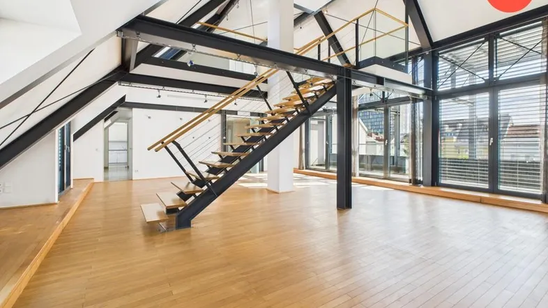 Geräumiger, heller Wohnbereich mit hohen Decken, Holzboden und offener Treppe zu einer Galerie.