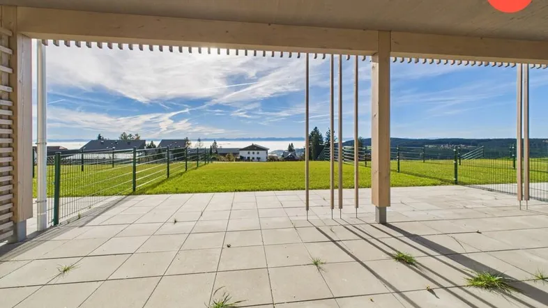 Große, geflieste Terrasse mit weitem Blick über grüne Felder und den Horizont unter blauem Himmel.