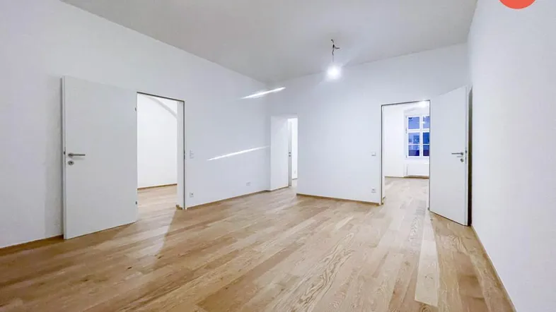 Helles, leeres Zimmer mit Holzboden und mehreren Türen, bereit für die individuelle Gestaltung.