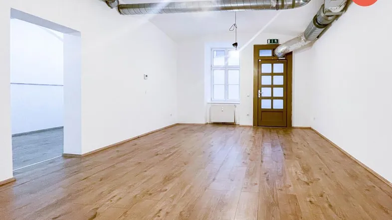 Heller Raum mit Holzboden, weißen Wänden und sichtbaren Lüftungsrohren an der Decke.