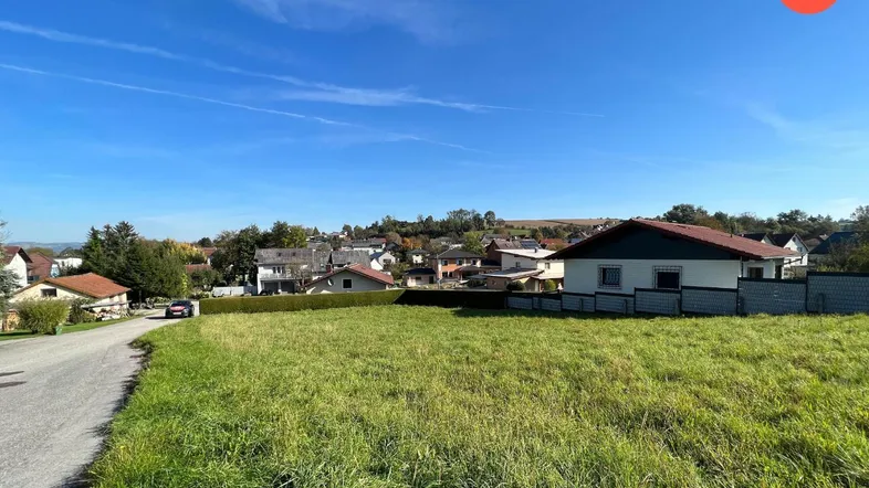 Weitläufiges Grundstück mit grüner Wiese und Blick auf die umliegende Wohnsiedlung unter blauem Himmel.