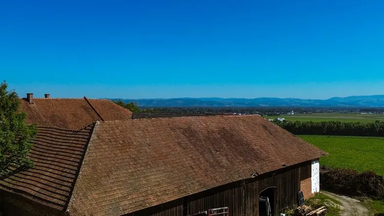 Luftaufnahme eines alten Bauernhofgebäudes mit Ziegeldach, umgeben von Feldern und ländlicher Landschaft.