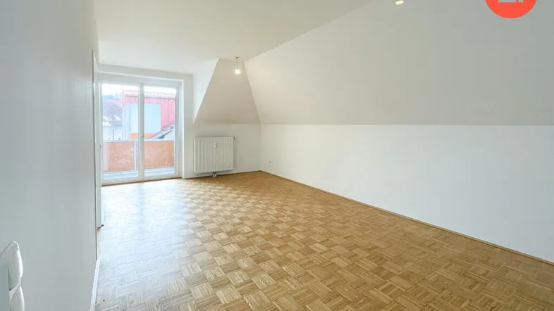 Helles Zimmer mit Parkettboden, Dachschräge und Zugang zu einem Balkon.