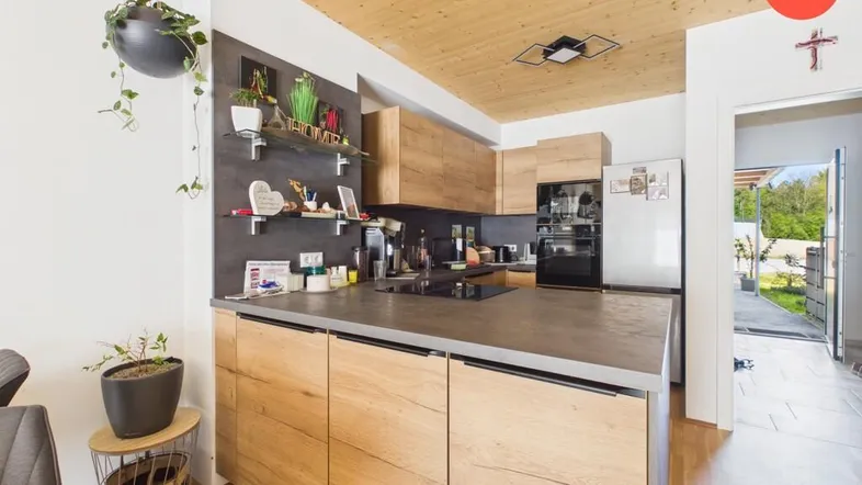 Moderne Küche mit Holzfronten, dunkler Arbeitsplatte und Zugang zum Gartenbereich.
