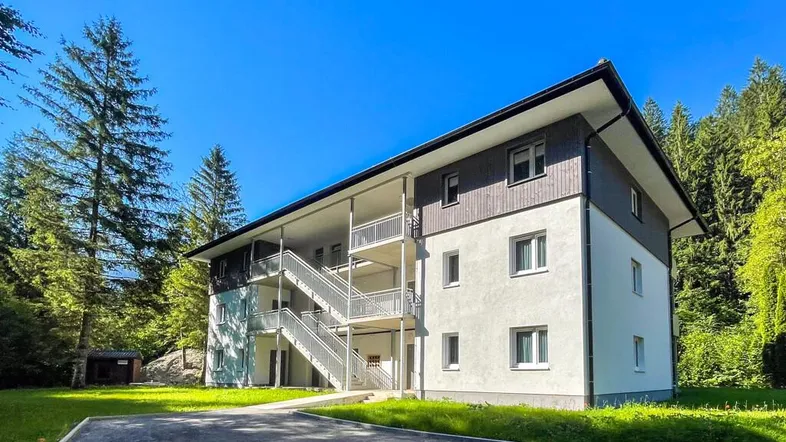 Modernes Mehrfamilienhaus mit Außentreppen und Balkonen, umgeben von grüner Natur und Bäumen.