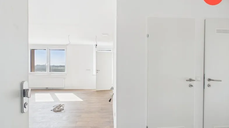 Heller, leerer Wohnbereich mit Laminatboden und Fenstern, die viel Tageslicht hereinlassen.