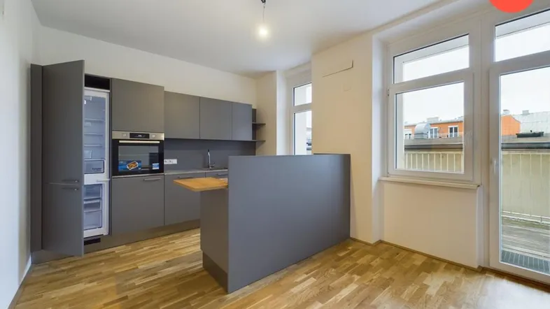Moderne Küche mit grauen Schränken, integrierten Geräten und Holzboden, mit Zugang zu einem Balkon.