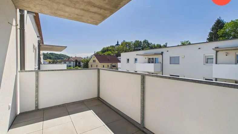 Heller Balkon mit Fliesenboden und Blick auf die umliegende Wohngegend und grüne Hügel.