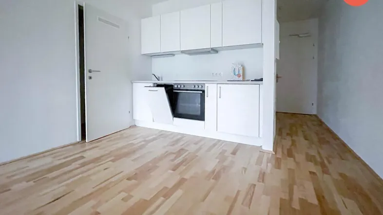 Helles Zimmer mit integrierter Küchenzeile und hellem Holzfußboden, ideal für ein Studio-Apartment.
