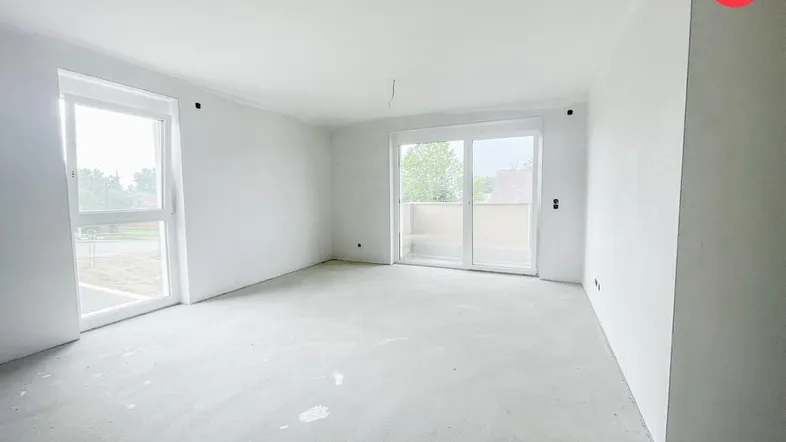 Helles, unmöbliertes Zimmer mit großen Fenstern und Zugang zu einem Balkon.