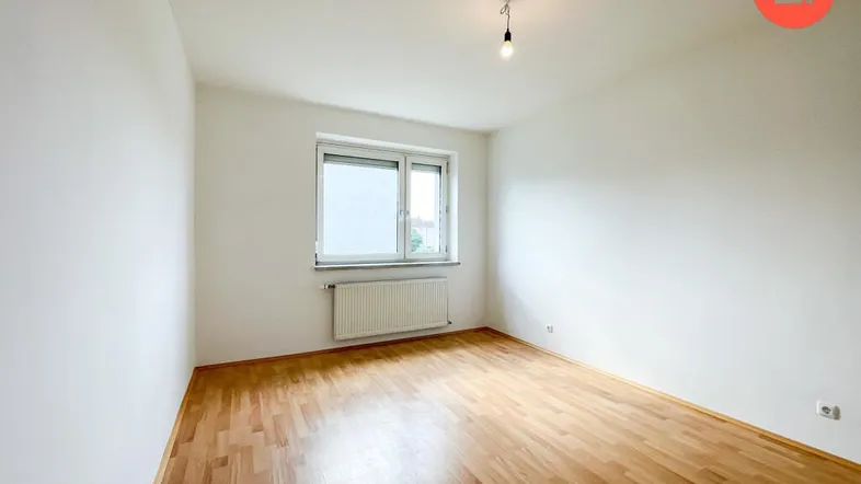 Helles Zimmer mit Parkettboden und großem Fenster, ideal als Wohn- oder Schlafbereich nutzbar.