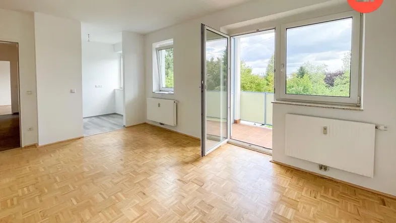 Helles Wohnzimmer mit Parkettboden, großen Fenstern und Zugang zum Balkon.