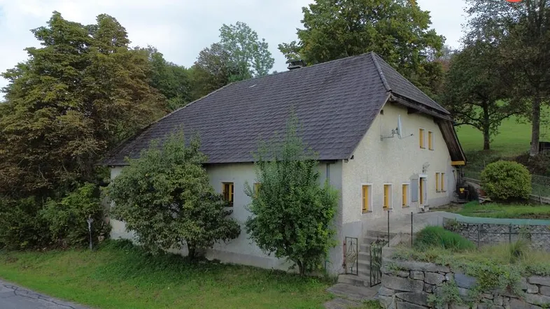 Ländliches Wohnhaus mit traditioneller Architektur, umgeben von Bäumen und grüner Landschaft.