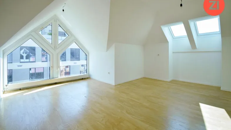 Helles Zimmer im Dachgeschoss mit großen Giebelfenstern, Dachfenstern und Holzfußboden.