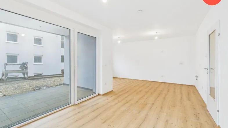 Heller, leerer Raum mit großen Glasfronten und Zugang zu einer Terrasse.
