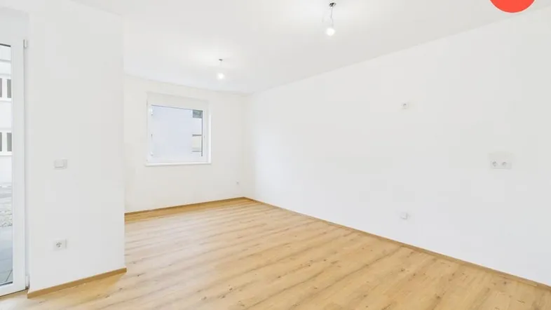 Helles, leeres Wohnzimmer mit Laminatboden und Zugang zu einem Außenbereich.