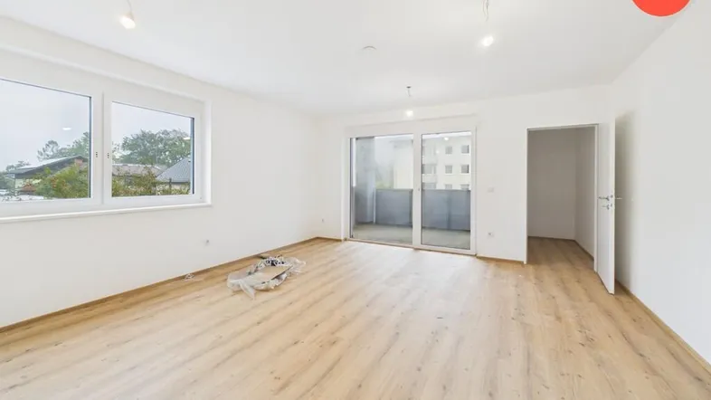 Helles, leeres Zimmer mit Holzboden und Zugang zu einem Balkon, ideal als Wohnbereich.