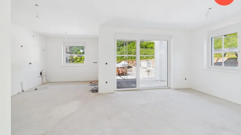 Helles, unmöbliertes Wohnzimmer in einem Neubau mit großen Schiebetüren zum Außenbereich und Blick ins Grüne.