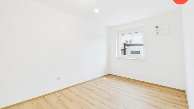 Helles, leeres Zimmer mit Laminatboden und einem Fenster, bereit für die individuelle Gestaltung.